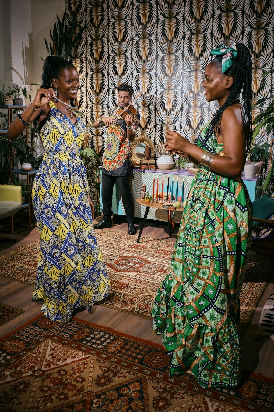 Two women dancing in African print dresses while a violinist plays
